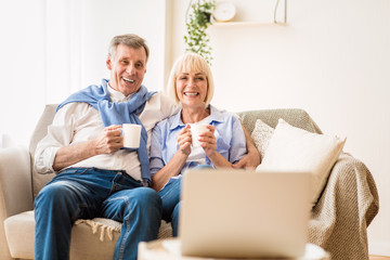 Mature couple watching film on laptop and drinking coffee