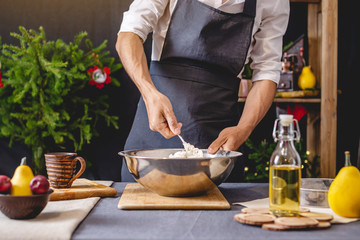 Man chef in a black apron kneading the dough with hands for Christmas baking. Joyful cooking for festive new year table