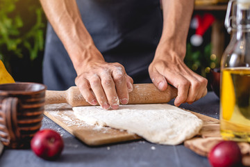 Man chef in a black apron kneads the dough with hands for Christmas baking. Joyful cooking for festive new year table