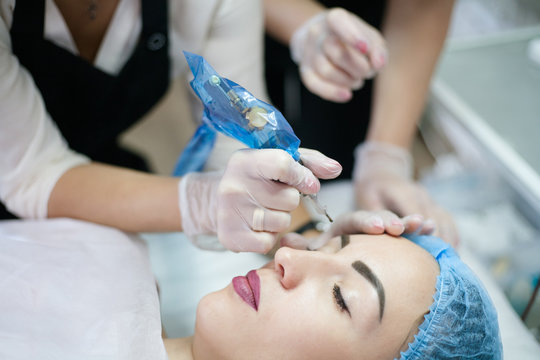 Permanent makeup class. Cropped shot of beautician teaching intern how to use tattoo machine for eyebrow microblading.