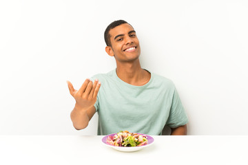 Young handsome man with salad in a table inviting to come
