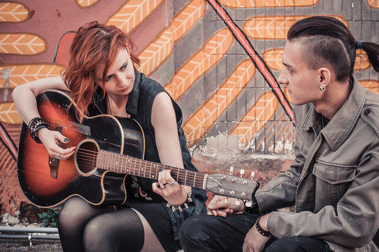 beautiful young red-haired girl plays the guitar for her boyfriend, street music culture concept