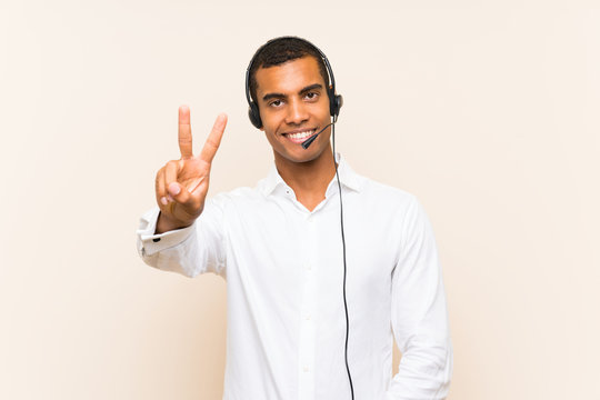Young brunette man working with a headset smiling and showing victory sign