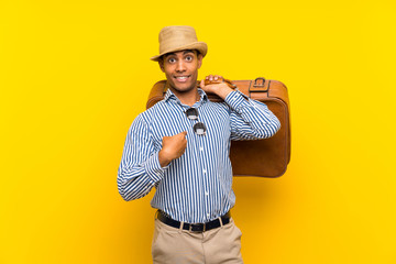 Brunette man holding a vintage briefcase over isolated yellow background with surprise facial expression