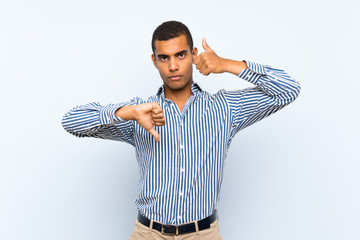 Young handsome brunette man over isolated blue background making good-bad sign. Undecided between...