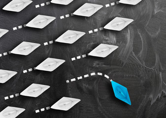 stepping out of the line or breaking new ground concept with group of paper boats going one way and...