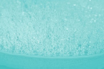 Fototapeta na wymiar Soap bath bubbles on turquoise background. Laundry detergent, suds textured pattern. White soap suds macro view, copy text. Abstract background textured effect of blue soap foam close-up.