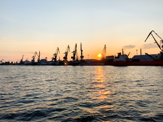 Naklejka premium River port with ships at sunset. Busy traffic artery. Logistics and infrastructure. Loading and unloading of ships, trade traffic. Industry and economics. Plants and factories. Transport hub. Dnipro