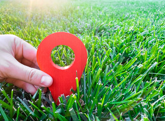 A hand is holding a red location marker in the green grass. The concept of tourism and travel....