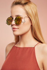 Close-up portrait shot of a young blonde European lady with straight long hair dressed in a ruddy top with thin shoulder-straps. The girl is wearing stylish circle sunglasses with lustrous rim,  © RedUmbrella&Donkey