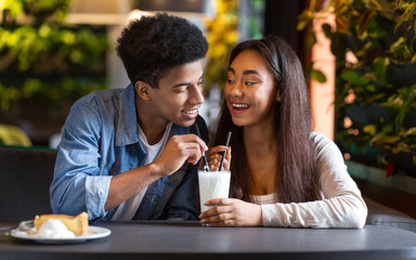 Cute couple of teenagers enjoying milkshake at cafeteria