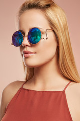 Close-up portrait shot of a young blonde European lady with straight long hair dressed in a ruddy top with thin shoulder-straps. The girl is wearing stylish circle sunglasses with lustrous rim, © RedUmbrella&Donkey