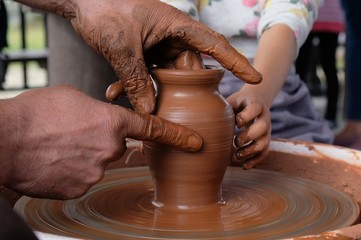 The potter teaches the child how to form a clay jug on a potter's wheel.
