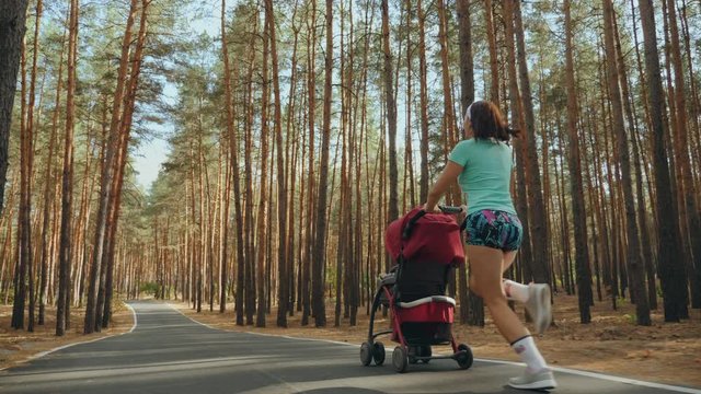 Rear view: Running woman with baby stroller enjoying a sunny summer day in a pine forest. Jogging or power walking supermom. Slow-motion 4k video