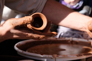 The potter teaches the child how to form a clay jug on a potter's wheel.