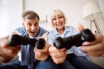 Excited mature couple playing video games at home © Prostock-studio
