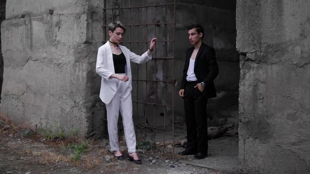 beautiful model couple fixes dressing and poses at rusty grate in old grey abandoned building slow motion