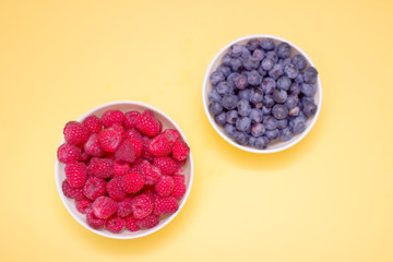 Forest berries, raspberries, blueberries in a bowl on a yellow background from above
