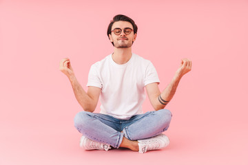 Image of young brunette man meditating with fingers together on floor