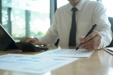 Young businessman is checking data on a graph and using a laptop on an office desk.