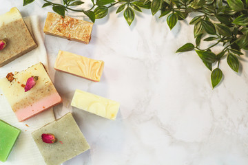 handmade craft soap different colors with herbs, flower petals. mint and rosebuds on a marble surface with green liana leaves on the side of flat lay. Spa treatment kit, body care with free space