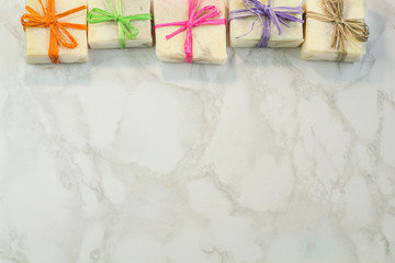 handmade organic soap in gift wax wrapping  paper with multi colored eco raffia ribbons on marble surface with space for text. Instagram style soap flat lay frame