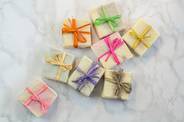 handmade organic soap in gift wax wrapping  paper with multi colored eco raffia ribbons on marble surface with space for text. Instagram style soap flat lay frame