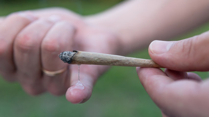 Close-up of males hands holding marijuana joint, smoking cannabis blunt outdoors.