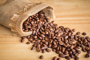 Roasted coffee beans in burlap sack on wood desk