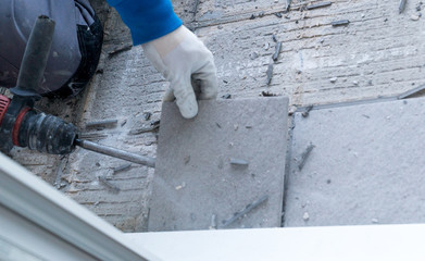 construction worker using a handheld demolition hammer and wall breaker to chip away and remove old...