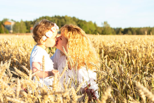 Mother and daughter hugging tenderly. A girl with red hair and a child sits on a wheat field. Kiss of the mother, countryside.