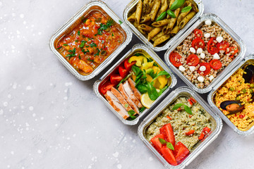Food delivery.Different aluminium lunch box with healthy natural food pasta pesto, spelt, paella, quinoa, chicken salad, curry.  airlines food. airline meals and snacks . takeaway 