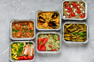 Food delivery.Different aluminium lunch box with healthy natural food pasta pesto, spelt, paella, quinoa, chicken salad, curry.  airlines food. airline meals and snacks . takeaway 