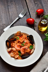 Spaghetti seafood pasta with clams and prawns with mussels and tomatoes in a white plate with on a wooden table. Recipe of Italian cuisine