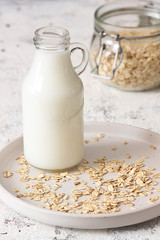 Oat flakes in glass jar and bottle of milk on white background