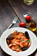 Spaghetti seafood pasta with clams and prawns with mussels and tomatoes in a white plate with on a wooden table. Recipe of Italian cuisine