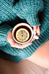Female hands holding mug of hot tea with lemon in morning.