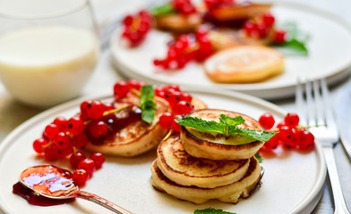 family breakfast pancakes gluten free with cherry jam and fresh berries,  two plates of pancakes, milk in round glasses.