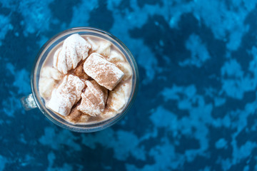  A glass of hot cocoa with marshmallows on a textured blue background. Top view. Copy space.