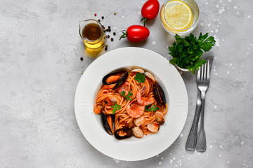 Pasta spaghetti with seafood mussels, shrimps, parsley.  In a white plate on a gray stone table, top view. Pasta recipe , Italy 
