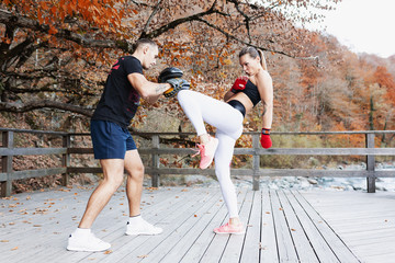 Obraz premium Female student and a male martial arts coach are engaged in kickboxing in protective gear in the open air. Concept of sports and stamina. Translation: Konstantin
