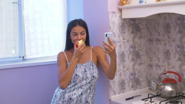 the girl eats an apple and speaks via video calling through the phone in the kitchen, after which, choking, she begins to choke and falls down the frame