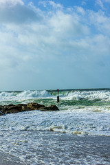 Fototapeta premium Crashing waves on a stony groyne (breakwater) during a massive storm under a majestic blue sky and white clouds