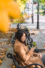 Obraz na płótnie Canvas young adult fashion woman sitting at city park bench in autumn fall season