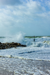 Crashing waves on a stony groyne (breakwater) during a massive storm under a majestic blue sky and white clouds