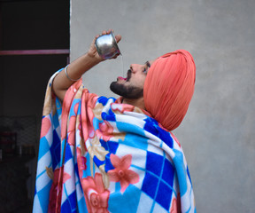 Naklejka premium An Indian Punjabi boy drinking water in village style in an Indian village