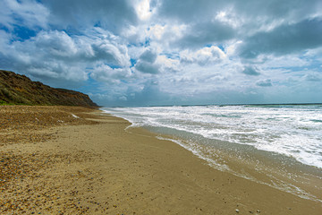 A view of a choppy and foamy sea along a sandy beach and cliff under a majestic stormy sky