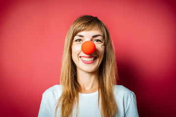 Young beautiful woman with a red nose of a clown on a pink background. Concept red nose day,...