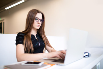 Woman marketing specialist working in internet via laptop computer, sitting in modern office space. Female experienced freelancer using applications on notebook. Entrepreneur keyboarding on netbook
