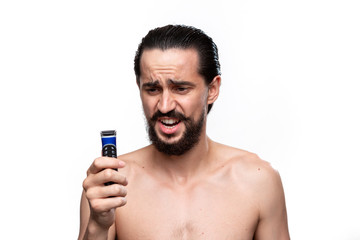 Fototapeta premium Excited bearded man with mustache holds electric shaver standning bare isolated over white background. Concept of morning treatment and shaving. Time to trim your beard.